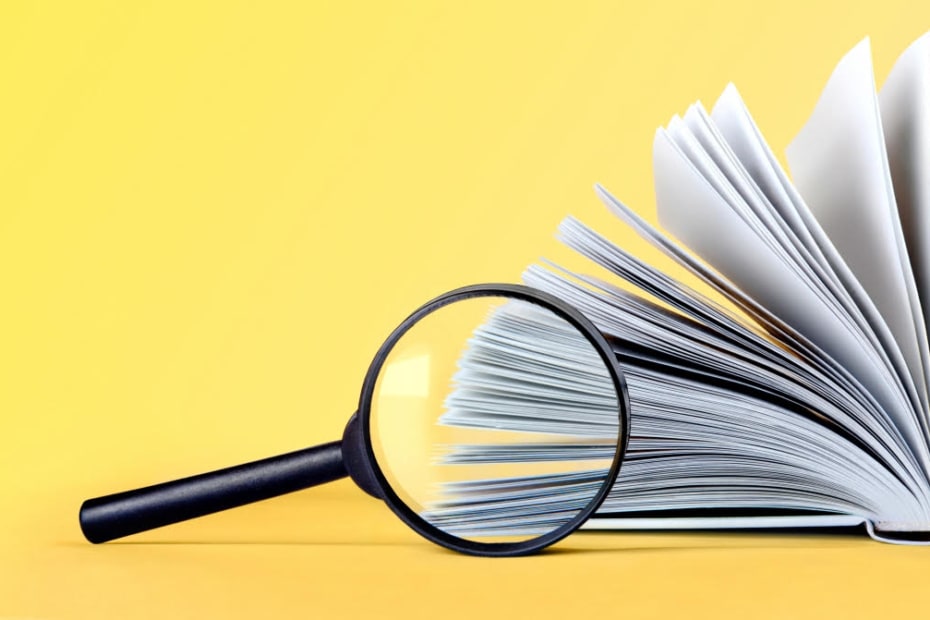 Book With Pages Fanned Out With Magnifying Glass In Front Of It