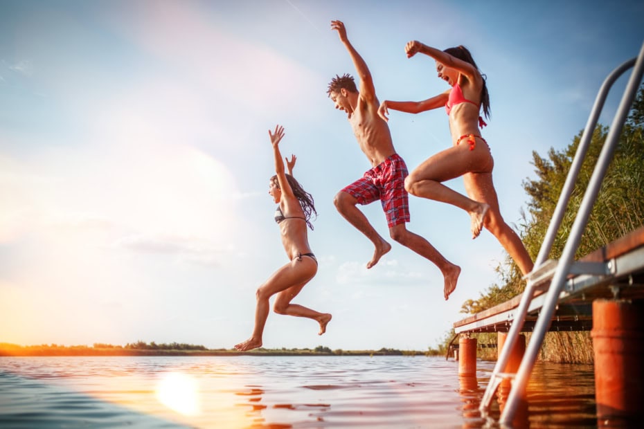 young people jumping off of a dock into a lake